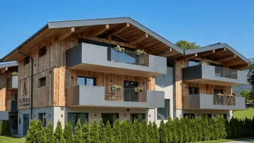Modernes Gebäude mit Holzfassade, grauen Balkonen und gepflegter Hecke.