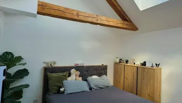 Gemütliches Schlafzimmer im Dachgeschoss mit sichtbaren Holzbalken und einem großen Dachfenster für viel Tageslicht.