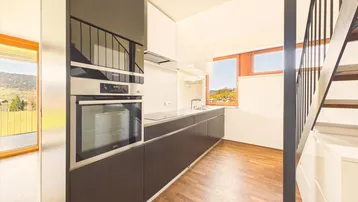 Moderne Küche mit dunklen Unterschränken, integriertem Backofen und Fenster mit Blick auf die grüne Landschaft.