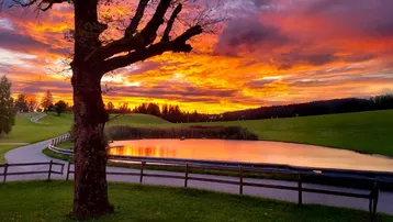 Spektakulärer Sonnenuntergang über einer idyllischen Landschaft mit Teich und grünen Wiesen.