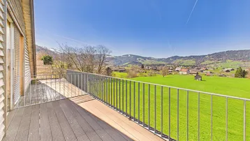 Geräumiger Balkon mit Holzdielen und Metallgeländer, der einen herrlichen Panoramablick auf die Berge und das Tal bietet.