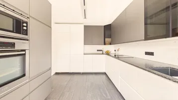 Moderne Küche mit weißen und grauen Schränken, integrierten Geräten und Fliesenboden.