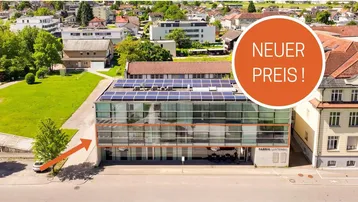 Luftaufnahme eines modernen Bürogebäudes mit Glasfassade, Solaranlage auf dem Dach und umliegender Wohnbebauung.