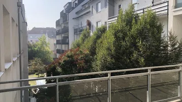 Balkon mit Blick auf einen grünen Innenhof und umliegende Wohngebäude.