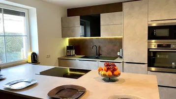 Moderne Küche mit Kücheninsel, integriertem Kochfeld und Backofen, sowie einem Fenster mit Blick ins Grüne.