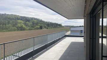Geräumige Terrasse mit weitem Blick über Felder und grüne Hügel unter strahlendem Himmel.