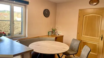 Gemütlicher Essbereich in der Küche mit Eckbank und rundem Holztisch, hell durch großes Fenster.