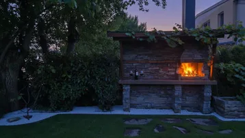 Gemütlicher Grillplatz im Garten bei Sonnenuntergang mit brennendem Feuer.