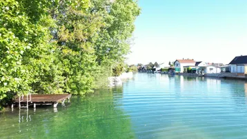 Idyllischer Kanalblick mit üppigem Grün und Häusern am Ufer unter blauem Himmel.
