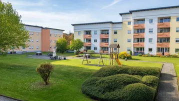 Mehrere Mehrfamilienhäuser mit großem Gemeinschaftsgarten und Kinderspielplatz.
