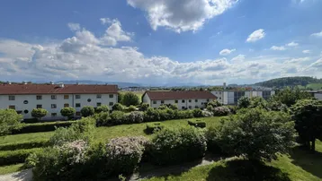 Weitblick über grüne Wohnanlagen und die umliegende Landschaft unter blauem Himmel.