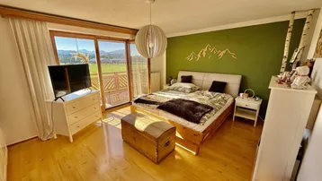 Helles Schlafzimmer mit Balkonzugang, Holzboden, grüner Akzentwand und Bergblick.