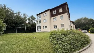 Mehrfamilienhaus mit gepflegter Grünfläche und Parkmöglichkeiten im Freien.