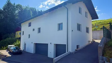 Modernes Einfamilienhaus mit weißer Fassade, Satteldach und integrierten Garagen.