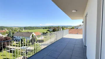 Geräumiger Balkon mit modernen Fliesen und weitem Blick über die umliegende Landschaft und Häuser.