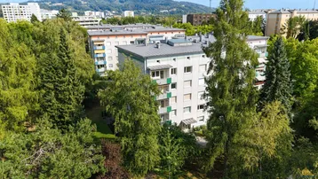 Mehrere Wohngebäude umgeben von üppigem Grün und Bäumen in einer städtischen Umgebung.