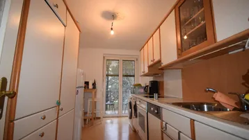 Schmale Küche mit Einbauschränken, Geräten und Zugang zu einem kleinen Balkon.