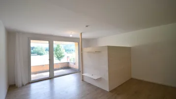 Helles Zimmer mit Holzboden und großem Fenster, das Zugang zu einem Balkon bietet.