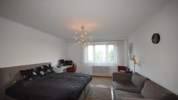 Helles Schlafzimmer mit großem Bett, Sofa und Arbeitsbereich am Fenster.