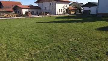 Großes grünes Grundstück mit Rasenfläche und Wohnhäusern im Hintergrund unter blauem Himmel.
