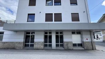 Vorderansicht eines weißen Gebäudes mit braunen Rollläden und einem grauen Vordach über dem Erdgeschoss.