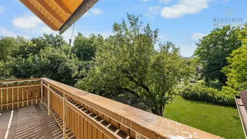 Blick vom Holzbalkon auf die umliegende grüne Landschaft und Bäume.
