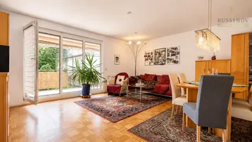 Heller Wohn- und Essbereich mit Parkettboden, rotem Sofa und Zugang zum Balkon.