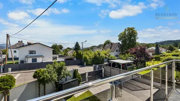 Ausblick vom Balkon auf die Nachbarschaft mit Häusern und grünen Hügeln im Hintergrund.
