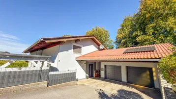 Vorderansicht des Hauses mit Doppelgarage, Carport und Photovoltaikanlage unter blauem Himmel.
