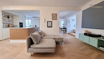 Helles, offenes Wohnzimmer mit Fischgrätparkett und integrierter Küche, ideal für modernes Wohnen.