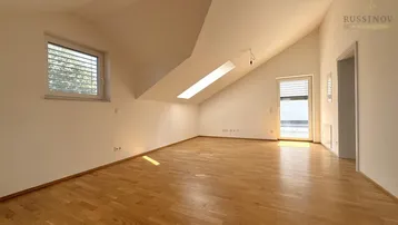 Helles Dachgeschosszimmer mit Holzboden, schrägen Wänden und Zugang zu einem Außenbereich.