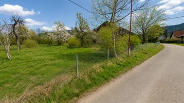 Grünes Grundstück mit blühenden Bäumen und Blick auf die umliegende Landschaft und Berge unter blauem Himmel.