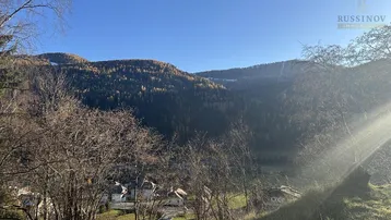 Weitläufiger Blick über das Tal und die umliegenden bewaldeten Berge unter strahlend blauem Himmel.