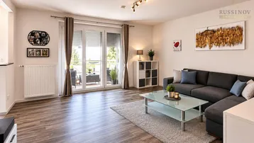 Helles Wohnzimmer mit modernem Sofa, Holzboden und Zugang zu einem sonnigen Balkon.