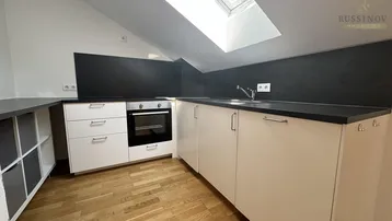 Moderne Küchenzeile im Dachgeschoss mit weißen Schränken, dunkler Arbeitsplatte und integriertem Backofen.