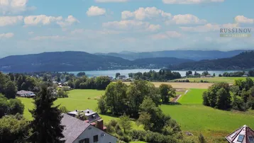 Panoramablick auf den Wörthersee mit umliegenden Hügeln und grüner Landschaft unter blauem Himmel.