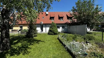 Gepflegter Gartenbereich hinter dem Haus mit Rasenfläche, Blumenbeeten und Blick auf die Rückseite des Gebäudes.
