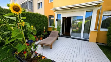 Helle Terrasse mit Sonnenliege und blühendem Garten, ideal zum Entspannen im Freien.
