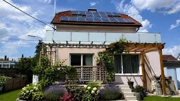 Rückseite des Hauses mit blühendem Garten, Terrasse und Solaranlage auf dem Dach.