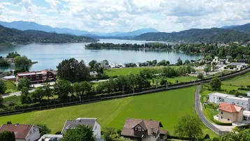 Panoramablick auf einen malerischen See, umgeben von Bergen und Wohngebieten unter blauem Himmel.