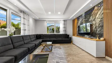 Modernes Wohnzimmer mit großem Ecksofa, stilvoller Marmorwand und indirekter Beleuchtung.