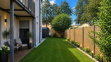 Langer, schmaler Gartenbereich mit Rasen, Bambuszaun und einer kleinen Terrasse mit Sitzgelegenheiten.