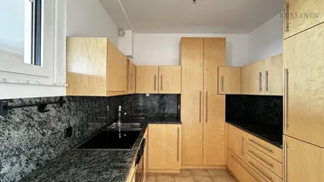 Funktionale Küche mit hellen Holzschränken, dunklen Granitarbeitsplatten und Fliesenboden.
