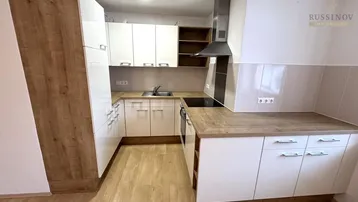 Moderne Küche mit weißen Hochglanzfronten, Holzoptik-Arbeitsplatten und integrierter Dunstabzugshaube.
