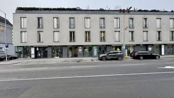 Modernes Geschäftsgebäude mit mehreren Ladenlokalen im Erdgeschoss und Wohnungen darüber, an einer Straße gelegen.