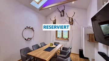 Gemütlicher Essbereich mit Holztisch, bequemen Stühlen, Geweih-Dekoration, Dachfenster und Blick ins Grüne.