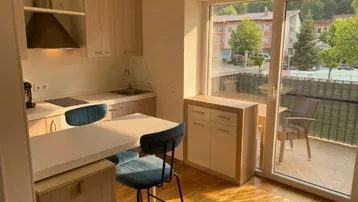 Helle Küche mit Holzelementen, integriertem Essbereich und Zugang zum Balkon.