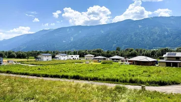 Weitläufige Landschaft mit Neubauten und majestätischem Bergblick unter blauem Himmel.