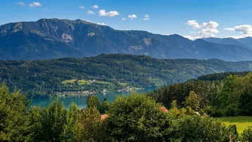 Panoramablick auf die majestätischen Berge, einen ruhigen See und dichte Wälder unter blauem Himmel.