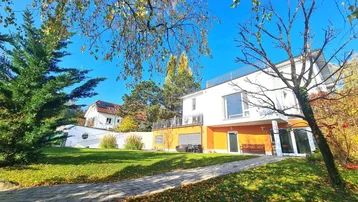 Großzügiger Gartenbereich mit gepflastertem Weg und moderner Hausfassade an einem sonnigen Herbsttag.